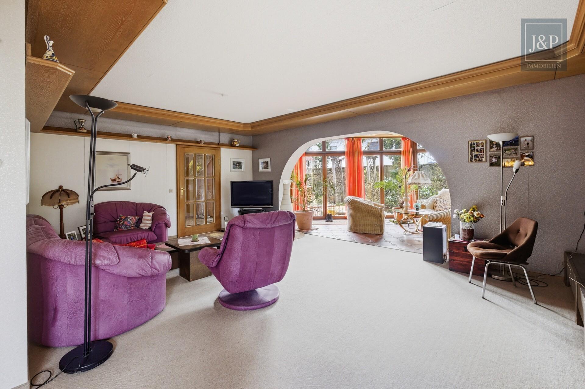 Zeitlose Eleganz der 70er: weitläufiger Bungalow mit Wintergarten-Oase und offenem Kamin - Wohnzimmer_Blick_Wintergarten